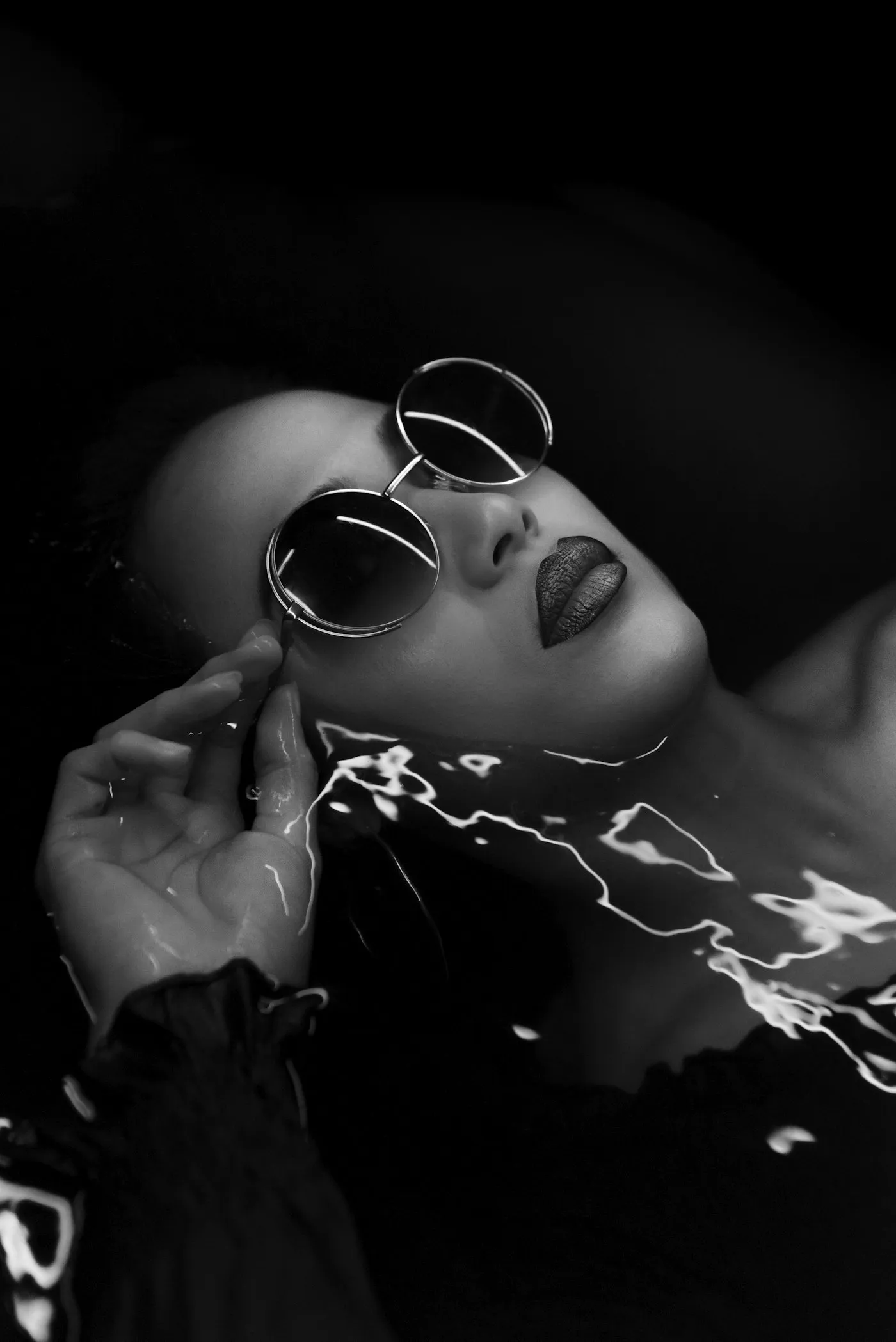 Black and white portrait with round sunglasses, rippling water reflections
